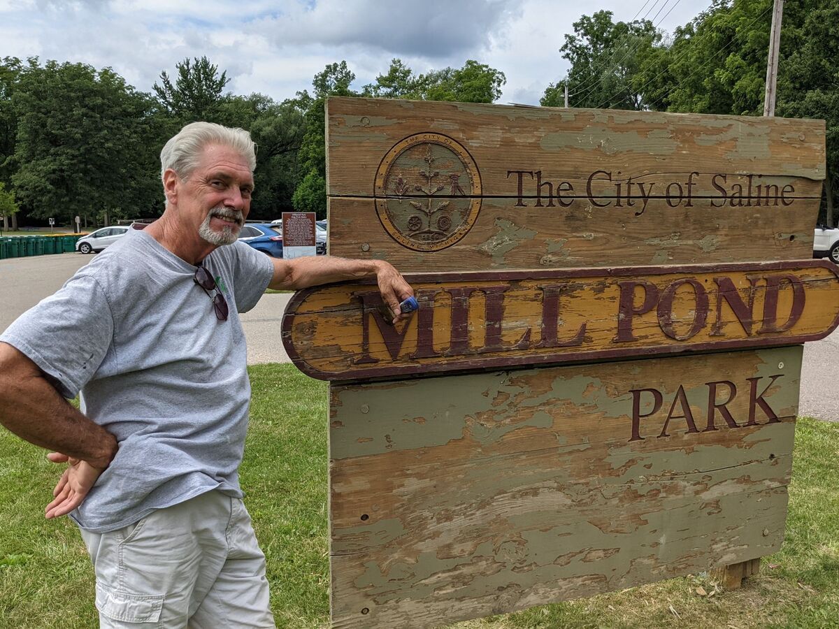Saline resident Jim Peters stands next to the sign at Mill Pond Park. He spent part of Saturday scraping, priming and painting the sign.